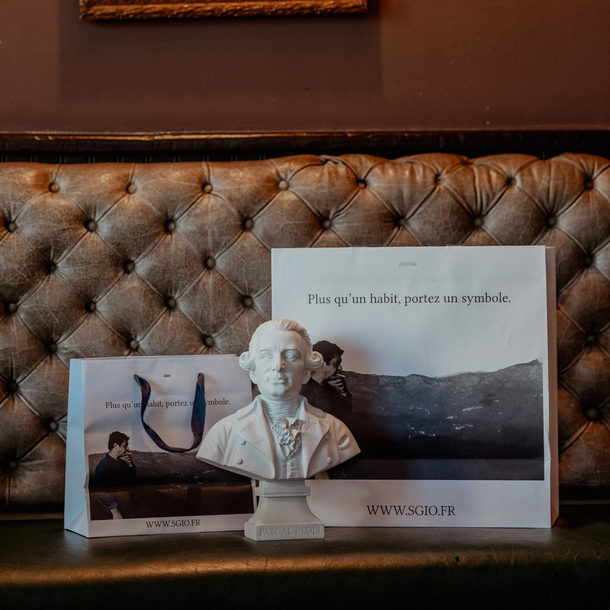 Sacs SGIÒ « Plus qu'un habit, portez un symbole » et buste de Pascal Paoli sur une banquette