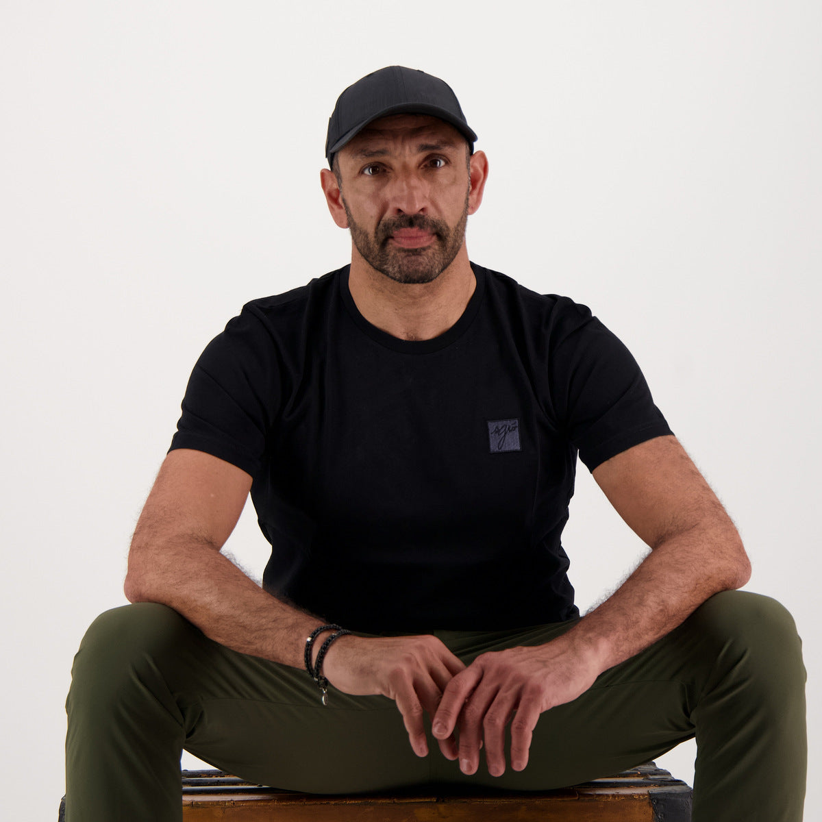 Homme assis portant le t-shirt classique noir SGIÒ, broderie sur le cœur