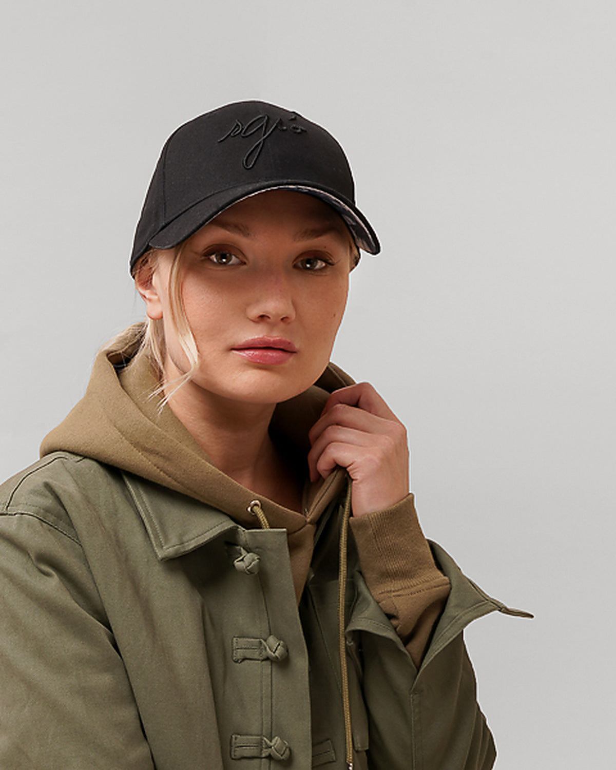 Casquette noire Sgiò portée, broderie ton sur ton, femme en veste kaki, studio